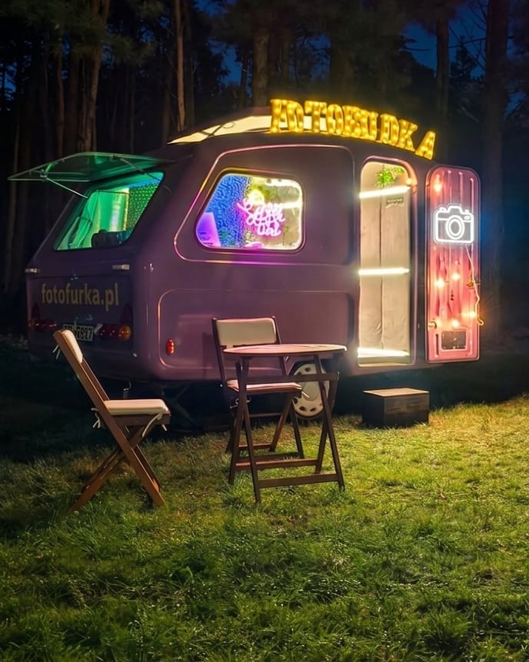 Fotofurka rozstawiona na trawie wieczorem, stolik i krzesełka przed przyczepą